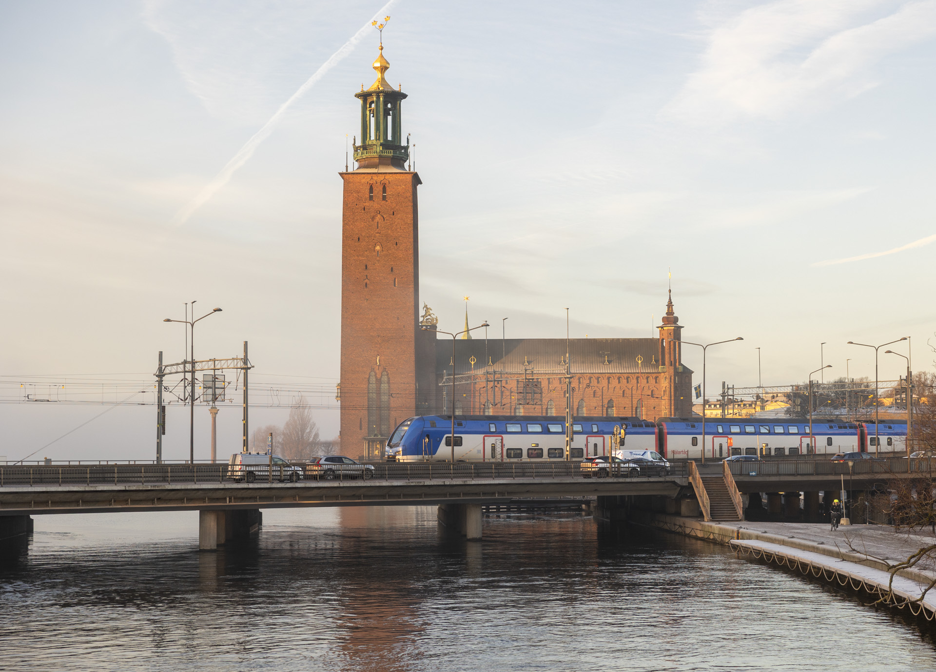 Stockholms stadshus med tornet i bakgrunden och ett Mälartåg på bron framför.