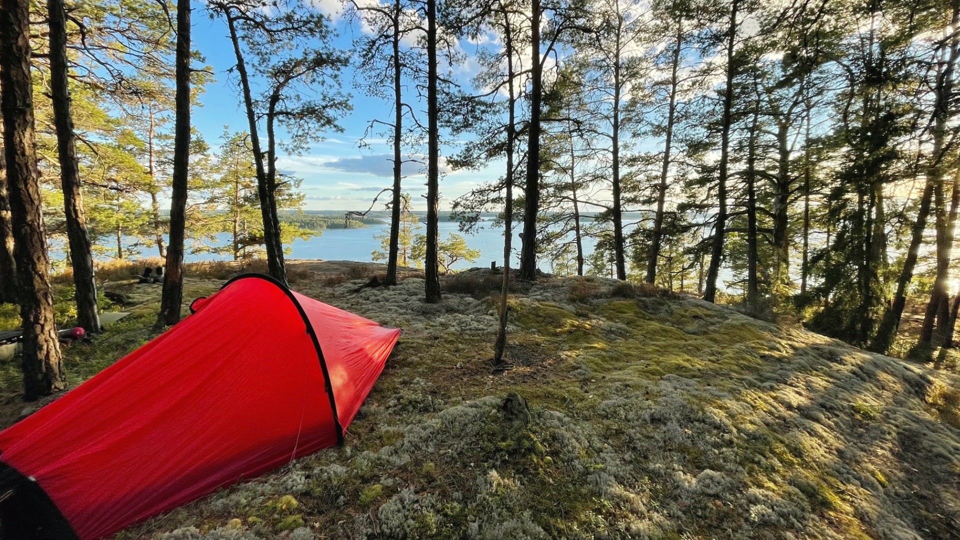 Ett rött tält på en bergsknall  i skogen med utsikt över vattnet